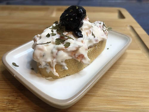 Aperirivo o canape con salmon ahumado y queso decorado con una oliva negra y perejil