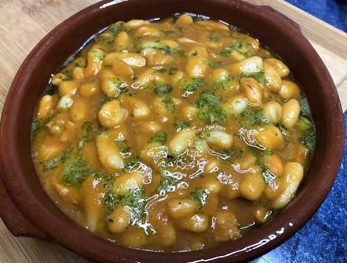 Cazuela de alubias con gambas servida con salsa verde por encima