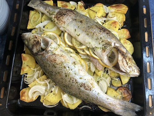 Lubina al horno con patatas y cebolla. Esta condimentada y rellena de limón.